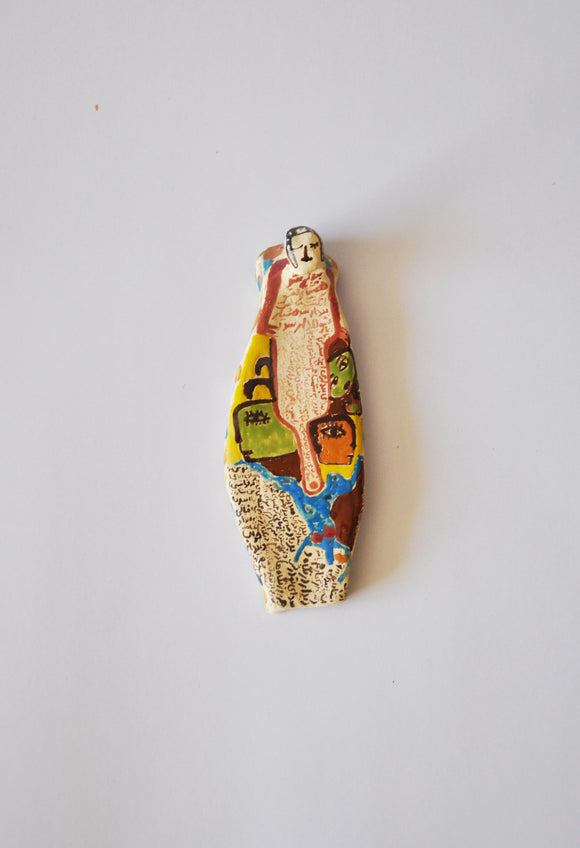 Elham Hemmat's 'Docile Bodies 2', a ceramic wall sculpture, measuring 12 cm x 5 cm x 1 cm. Photographed mounted on the wall. Contains colours of yellow, blue, green and orange.