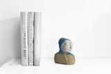Title: Angelic Artist: Sally Fitchard Medium: clay bust sculpture Size: 13.5 cm x 11.6 cm x 7.4 cm (in situ; on a book-shelf with books)