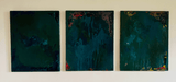 Three abstract paintings in shades of green and blue on a white wall