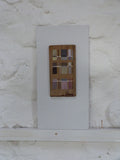 Abstract art piece on wood, mounted on a white board against a white washed stone wall