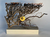 Artistic metal sculpture resembling a tree with a gold center on a gray background