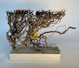 Sculpture of intertwined branches with a golden disk in the center on a stone base

