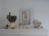 White dresser with ceramic items and a colorful abstract painting on a white wall.
