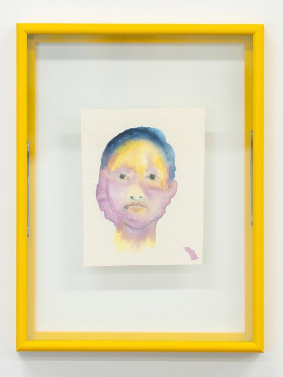 Framed artwork of a stylized face with a yellow frame on a white wall