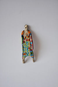 Elham Hemmat's 'Docile Bodies 5' a ceramic wall sculpture, measuring 14cm x 5cm x 1cm. Artwork contains colours of blue, green, orange and red. Photographed mounted on a wall.
