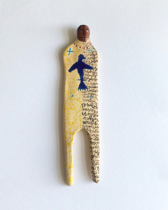Elham Hemmat's 'Docile Bodies 7' a ceramic wall sculpture, measuring 17cm x 4cm x 1cm. Artwork contains colours of yellow and blue. Photographed mounted on the wall.