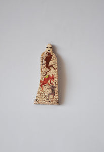 Elham Hemmat's 'Docile Bodies 8' a ceramic wall sculpture, measuring 17cm x 4cm x 1cm. Artwork contains colours of red, brown and cream. Photographed mounted on the wall.