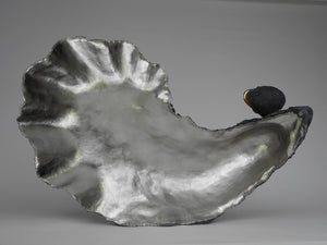 Lucy Gray's 'Shell IV' is a large-scale sculpture depicting an oyster shell with a smaller mollusk on its side. The artwork is made from jesmonite and gilded with palladium while the smaller mollusk is gilded with gold leaf.